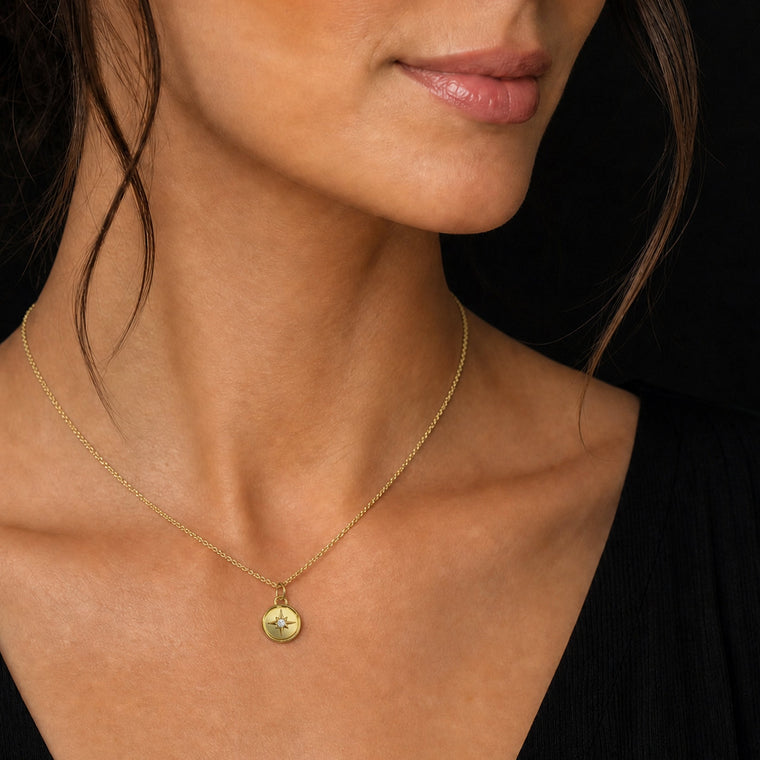 Close-up of a woman wearing a gold necklace with a pendant against a black background