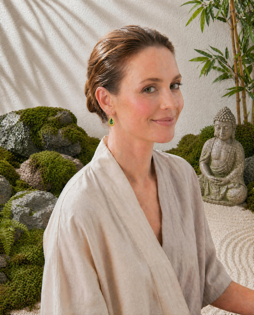 Woman in a white robe standing in front of a Zen garden with a statue and wearing tsavorite earrings.